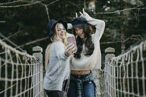dois feliz jovem mulheres em uma suspensão ponte levando uma selfie foto
