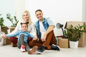 feliz família sentado em de madeira chão. pai, mãe e criança tendo Diversão junto. comovente casa dia, Novo casa e Projeto interior conceito foto