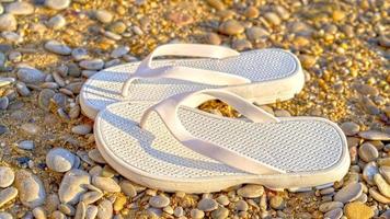 sapatos de praia brancos em um fundo de areia e seixos foto