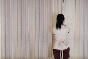 empregada doméstica fechando as cortinas da janela do quarto de hotel foto