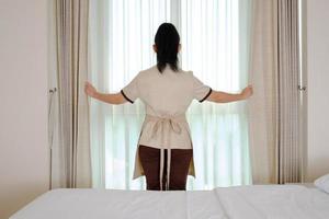 jovem empregada abrindo cortinas em quarto de hotel foto