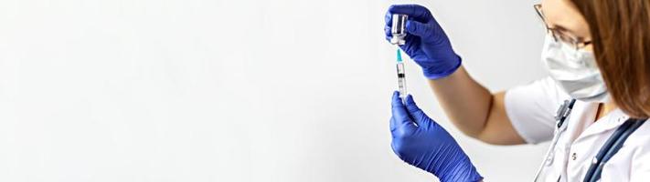 uma médica usando uma máscara médica injeta a vacina contra o coronavírus em uma seringa na clínica. O conceito de vacinação, imunização, prevenção contra covid-19.