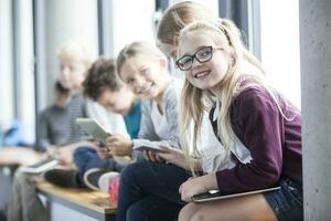 sorridente alunos com comprimidos em escola corredor foto