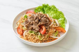 Salada picante de macarrão instantâneo com carne de porco no prato branco - comida asiática foto