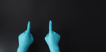 dois mão é vestem azul médico luvas e ponto a dedo em Preto fundo. foto