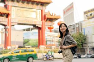 jovem ásia mulher mochila viajante desfrutando China Cidade rua Comida mercado dentro Bangkok, tailândia. viajante verificação Fora lado ruas. foto