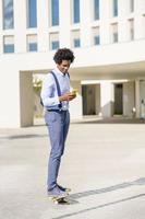 empresário negro em um skate olhando para seu smartphone ao ar livre. foto
