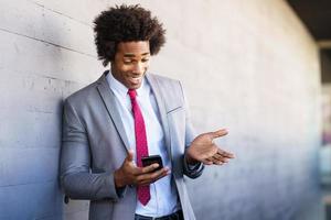 empresário negro usando um smartphone perto de um prédio comercial foto