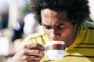 homem negro tomando café em um café enquanto está sentado à mesa ao ar livre foto