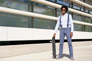 homem negro em pé ao lado de um prédio de escritórios com um skate.
