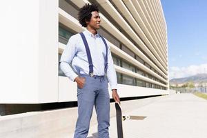 homem negro em pé ao lado de um prédio de escritórios com um skate.