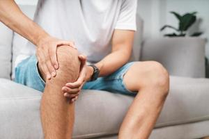 o homem que sofre de dor no joelho, sentado no sofá. foto