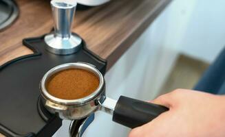 a barista mão detém uma suporte com terra fresco café para fazer café dentro uma café máquina. fechar-se. seletivo foco. foto