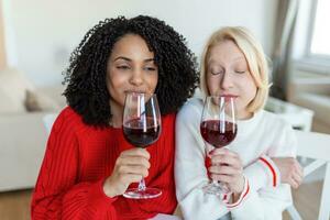 dois fêmea amigos gastos Tempo juntos às lar, sentado em sofá. cópia de espaço. alegre mulheres bebendo vinho foto