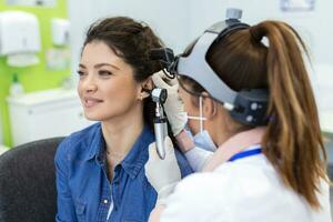 fechar acima do uma fêmea médico cuidadosamente segurando a orelha do dele paciente para estabelecer uma mais claro Visão do a dentro do dele orelha, para Vejo E se ele requer audição Auxilia às uma moderno clínica foto