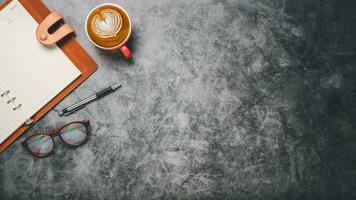 Sombrio escritório escrivaninha com caderno, caneta, óculos e copo do café, topo Visão com cópia de espaço, plano deitar.. foto