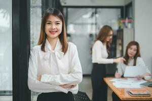 feliz o negócio mulher em pé competentemente e sorridente dentro aberto plano escritório com embaçado colega suposições sentado dentro escritório Como fundo, o negócio conceito. foto