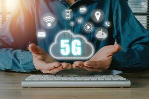 global comunicação rede conceito, pessoa mão segurando 5g ícone em virtual tela em escritório escrivaninha fundo, mundo Largo negócios, alta velocidade Móvel Internet, Novo geração redes. misturado meios de comunicação. foto