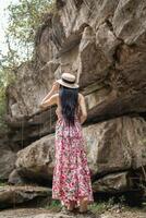 jovem mulheres turista dentro vintage vestir carrinhos sozinho em Rocha de cascata dentro a floresta na esperança para legal baixa para nadar. a costas do jovem ásia mulheres turista quem goza jogando dentro cascata sozinho. foto