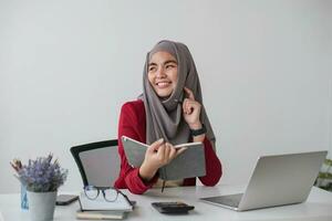 retrato do lindo muçulmano empresária sorridente às a Câmera, sentado às dela escrivaninha. foto