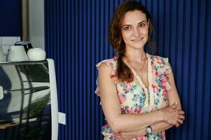 confiante retrato do uma o negócio mulher proprietário do uma cafeteria em pé contra uma azul parede dentro dela próprio cafeteria sorridente enquanto posando para a Câmera foto