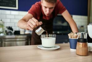 suave foco em derramando quente café para dentro açoitado leite contra borrado fundo do bonito barista atrás Barra contador foto