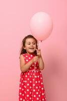 linda aniversário bebê menina regozija-se olhando às Rosa balão dentro dela mãos, alegremente sorrisos posando em Rosa fundo com cópia de espaço para anúncio. feliz infância e crianças proteção dia conceito foto