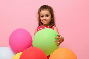 adorável lindo criança, bebê garota, 4 anos criança abraçando colorida balões, isolado sobre Rosa fundo com cópia de espaço. aniversário evento conceito, feliz mulher dia, crianças proteção dia. foto