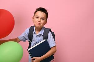 conceitos do feliz costas para escola. estudante com mochila segurando livro e multicolorido balões, fofa sorridente posando para Câmera sobre Rosa fundo com cópia de espaço foto