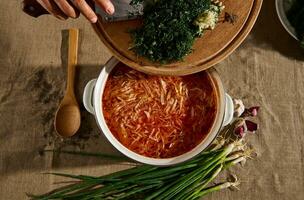 topo Visão a mãos do a chefe de cozinha derramar picado fresco aneto e alho para dentro uma Panela do recentemente preparado tradicional ucraniano sopa - borscht. ucraniano nacional cozinha foto