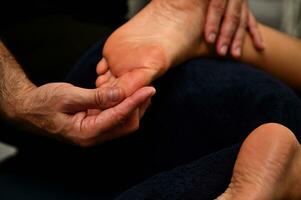 reflexologista aplicando pressão para pé com polegares. fechar acima do do terapeuta mãos massageando fêmea pé. foto