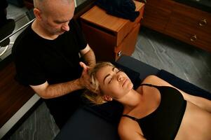 lindo mulher deitado em massagem mesa com olhos fechadas e recebendo profissional médico terapêutico cabeça massagem dado de massagista às saúde spa foto