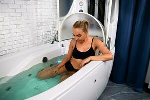 Alto ângulo Visão do uma mulher com perfeito corpo recebendo não invasivo anti-envelhecimento, anti-celulite tratamento dentro banheira do aberto spa cápsula foto