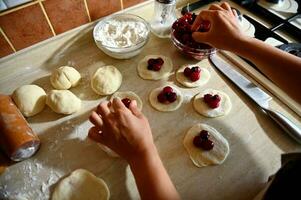 topo Visão do fêmea mãos colocando cereja bagas em uma volta forma do massa, o preenchimento ucraniano tradicional dumplings. processo do cozinhando dumplings degrau de degrau dentro a cozinha foto