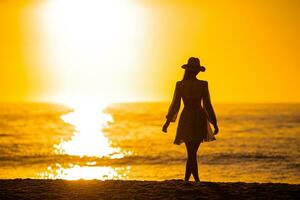 jovem mulher bonita no chapéu de palha na praia ao pôr do sol foto