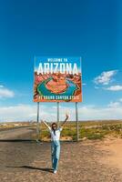 lindo mulher em dela viagem para a EUA em a fundo do bem-vinda para Arizona Estado fronteira placa certo dentro a paje desfiladeiro, EUA foto