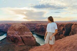 feliz menina em a Beira do a penhasco às ferradura banda desfiladeiro dentro página, arizona. aventura e turismo conceito. lindo natureza dentro EUA foto