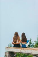 costas Visão do jovem meninas sentar em uma terraço às uma altura dentro a montanhas contra a pano de fundo do névoa e montanhas foto