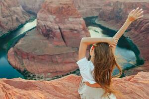 feliz menina em a Beira do a penhasco às ferradura banda desfiladeiro dentro página, arizona. aventura e turismo conceito. lindo natureza dentro EUA foto