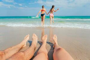 fechar-se do a pés do família em a branco arenoso de praia. crianças jogar em a de praia dentro raso água em verão período de férias foto