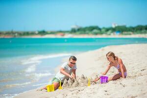 pai com filha jogando com areia em tropical de praia. família jogando com de praia brinquedos foto