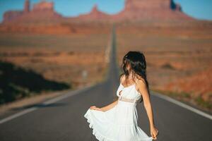 feliz jovem mulher dentro branco vestir em a famoso estrada para monumento vale dentro utah. surpreendente Visão do a monumento vale. foto