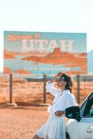 lindo mulher em dela viagem de a carro em a fundo do bem-vinda para Utah Estado fronteira placa certo dentro a monumento vale foto