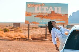 lindo mulher em dela viagem de a carro em a fundo do bem-vinda para Utah Estado fronteira placa certo dentro a monumento vale foto