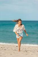 adorável jovem menina apreciar tropical de praia período de férias. a menina em a Beira Mar corre e ter Diversão foto