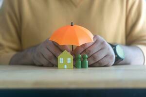 homem mão segurando laranja guarda-chuva cobrir de madeira casa modelo e de madeira humano modelo. foto