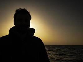 silhueta de um homem em pé contra o pôr do sol perto do mar foto