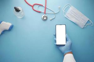 mão do médico segurando um telefone inteligente com tela em branco na mesa da clínica foto