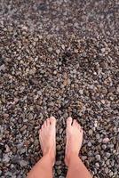 pés femininos descalços em praia de seixos, vista de cima