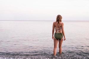 vista traseira de uma jovem em pé na praia pedregosa, olhando para o mar foto